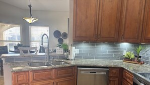 A kitchen with wooden cabinets, a Bosch dishwasher, a granite countertop, and a backsplash. - Sun-Soaked SW Cape Coral Gulf Access Retreat (Cape Coral)