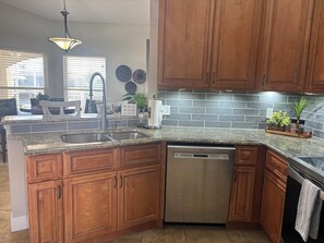 A kitchen with wooden cabinets, a Bosch dishwasher, a granite countertop, and a backsplash. - Sun-Soaked SW Cape Coral Gulf Access Retreat (Cape Coral)