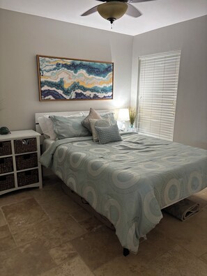 A bedroom with a bed, a nightstand, a lamp, a window with blinds, and a ceiling fan. - Sun-Soaked SW Cape Coral Gulf Access Retreat (Cape Coral)