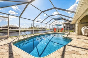A swimming pool with a clear view of the surrounding landscape, a covered area with a roof, and a body of water in the background. - Sun-Soaked SW Cape Coral Gulf Access Retreat (Cape Coral)