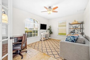 A living room with a ceiling fan, a television, a grey sofa, a patterned rug, and a wooden chair. - Sun-Soaked SW Cape Coral Gulf Access Retreat (Cape Coral)
