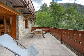 Ein Steinhaus mit Holzbalkon, einem Picknicktisch und einem Liegestuhl.