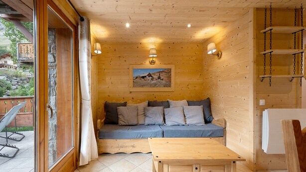 Ett mysigt rum med ett träpanelat tak, en soffa med kuddar, ett litet bord och en tavla på väggen.