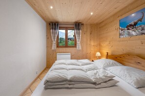 Ein Schlafzimmer mit Holzboden, einem Bett mit weißer Bettwäsche, einem Fenster mit Vorhängen und einer Wand-Klimaanlage.