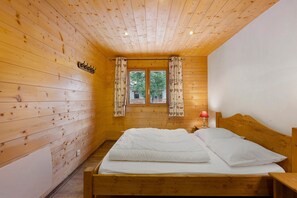 A wooden cabin room with a bed, a window with curtains, and a wall-mounted light. - Apartment for 11 Guests "Chalet le Caribou" with Mountain View and Balcony (Bonneval-sur-Arc)