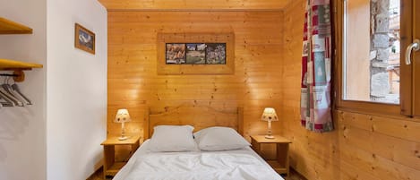 A wooden cabin room with a bed, two bedside tables, a window with curtains, and a picture on the wall.