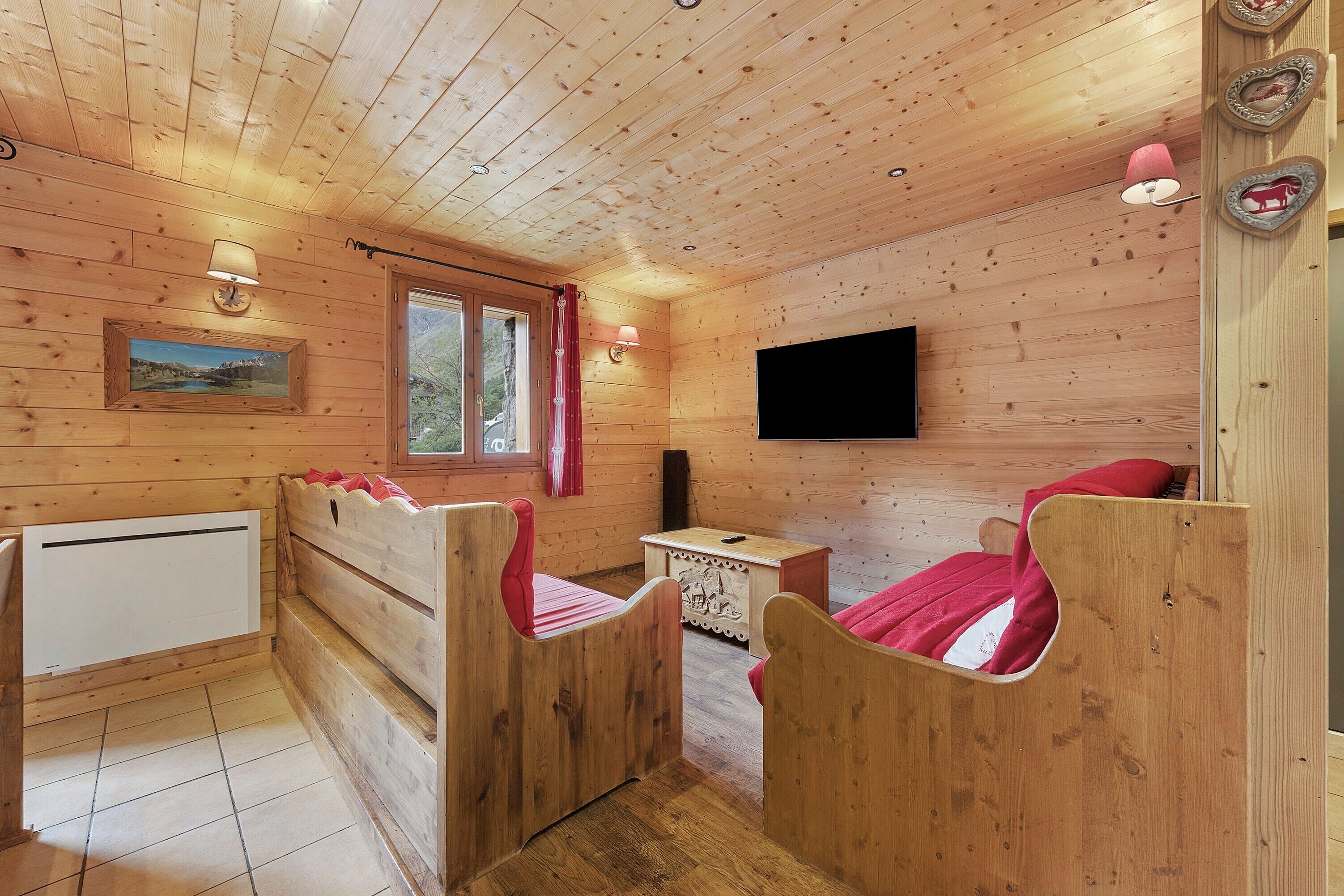 Una habitación de cabaña de madera con una cama, una mesita, un televisor y una ventana con cortinas.