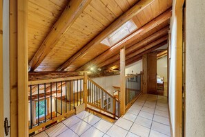 A wooden staircase leading to a lofted room with a view of greenery outside. - Chalet Le Caribou Apartment for 10 with Mountain View, Balcony, and Wi-Fi (Bonneval-sur-Arc)