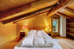 A cozy wooden bedroom with a sloped ceiling, a large bed with white bedding, two bedside lamps, and a view through an open door. - Chalet Le Caribou Apartment for 10 with Mountain View, Balcony, and Wi-Fi (Bonneval-sur-Arc)