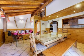 Um interior de madeira com mesa de jantar de vidro, cadeiras de madeira, um sofá e uma área de cozinha.