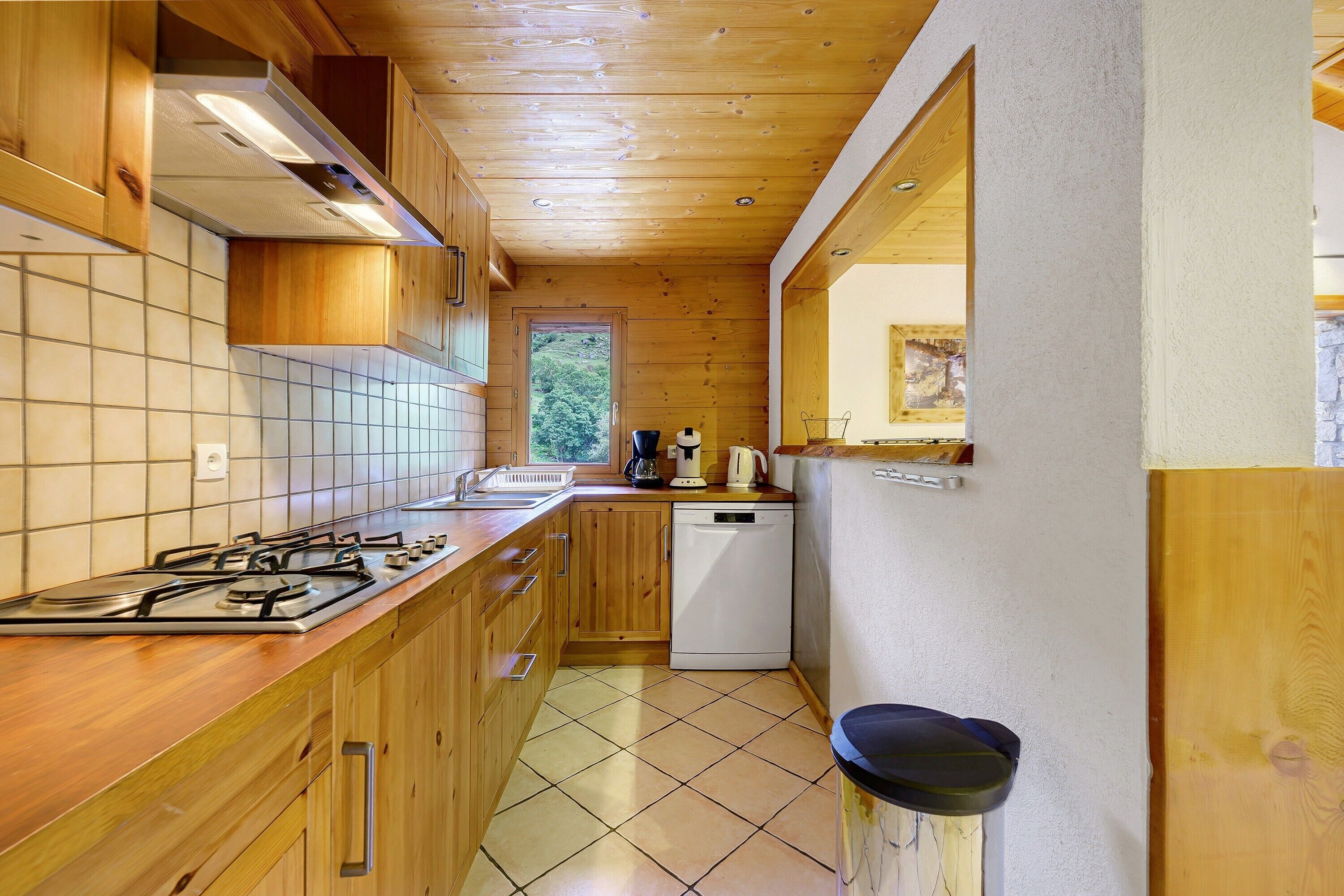 Una cucina compatta con mobili in legno, un fornello a gas, una lavastoviglie e una finestra che si affaccia sul verde.