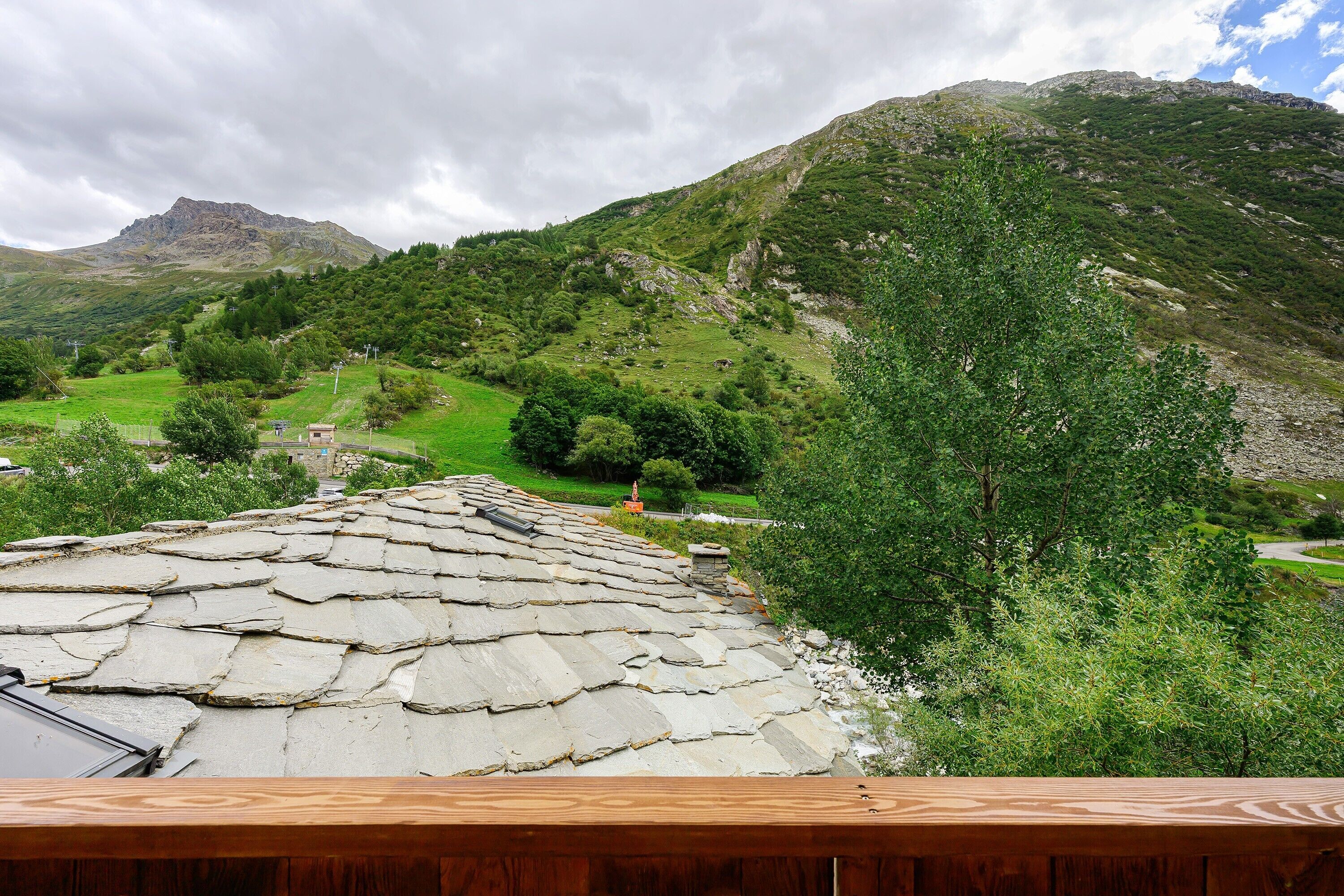 Un paisaje montañoso con un edificio de techo de piedra, vegetación exuberante y un cielo despejado.