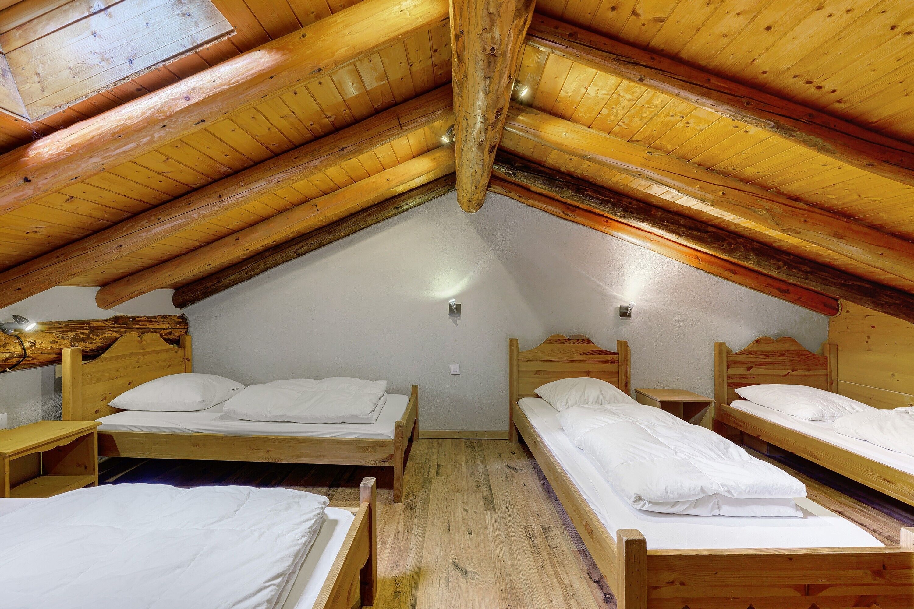 A room with three wooden beds arranged in a corner, a sloped ceiling, and a small table.