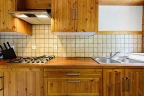 A kitchen with wooden cabinets, a gas stove, a sink, and a window above the countertop. - Chalet Le Caribou Apartment for 10 with Mountain View, Balcony, and Wi-Fi (Bonneval-sur-Arc)