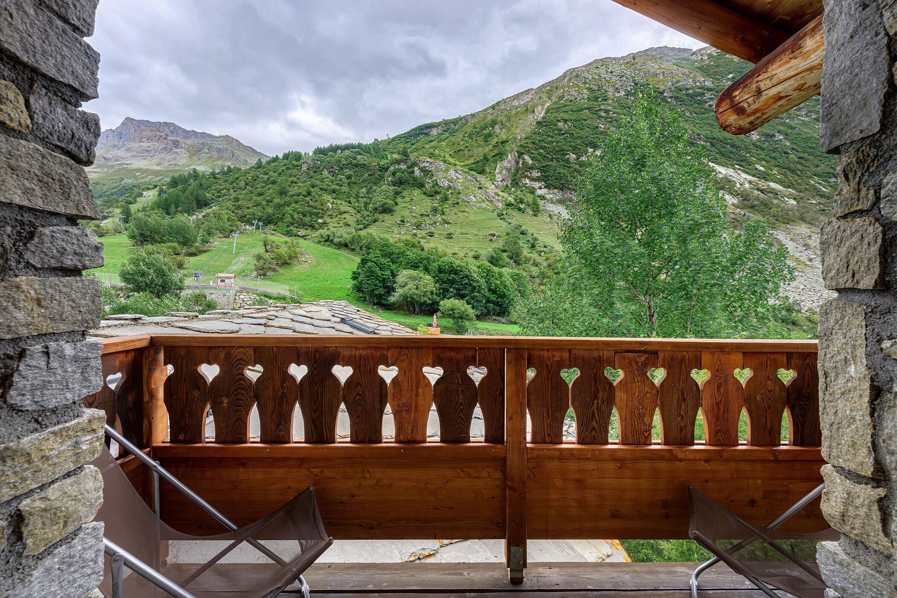 En træterrasse med hjerteformede udskæringer, der udover et bjergrigt landskab med grønt og en klar himmel.