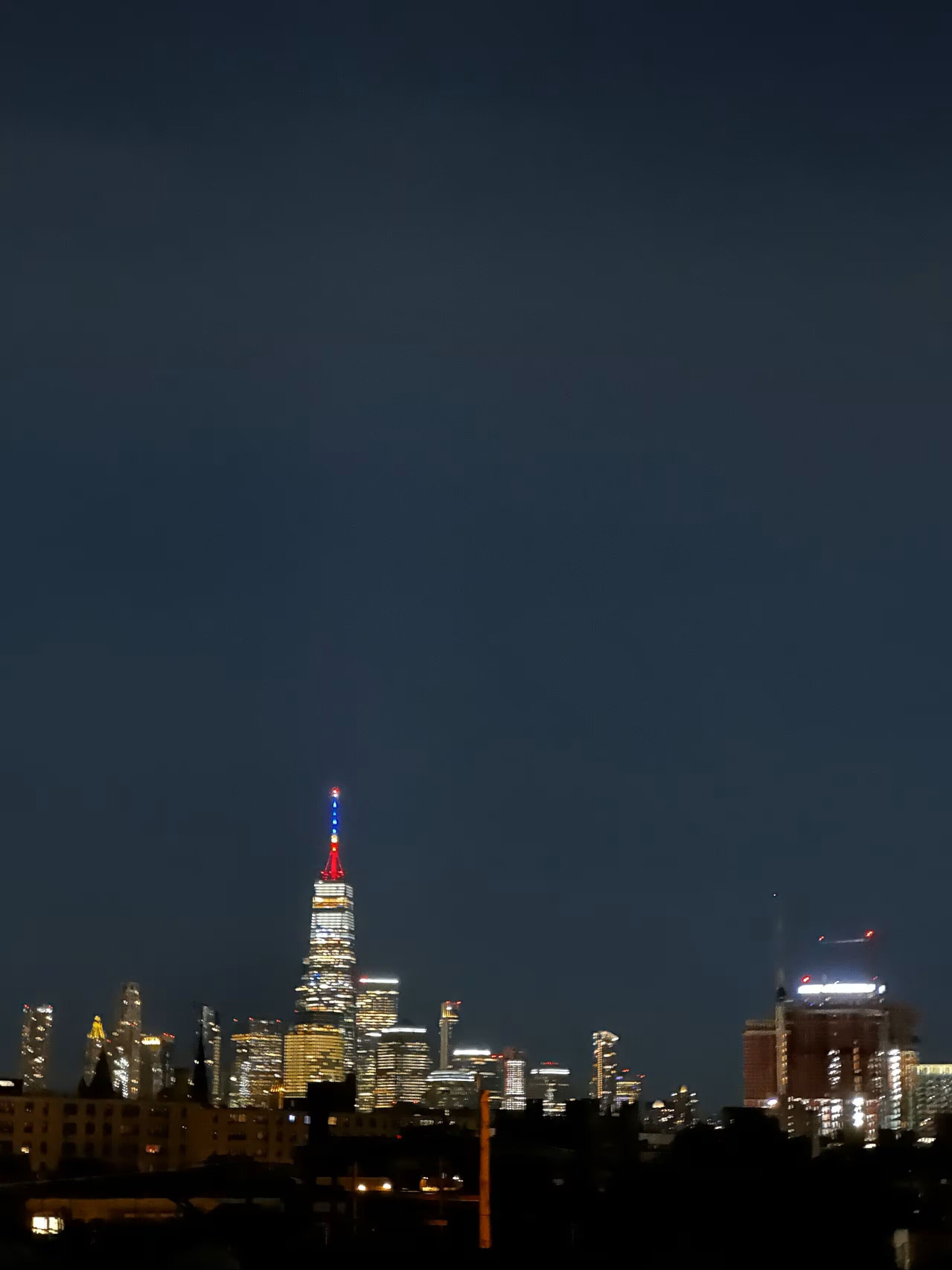 A city skyline at night with illuminated buildings, including a prominent tower with a red and blue light at the top.
