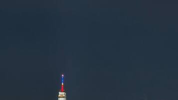 A city skyline at night with illuminated buildings, including a prominent tower with a red and blue light at the top.