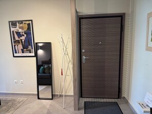 Una entrada moderna con una puerta de madera oscura, un cuadro abstracto enmarcado, un perchero blanco y un tapete pequeño.