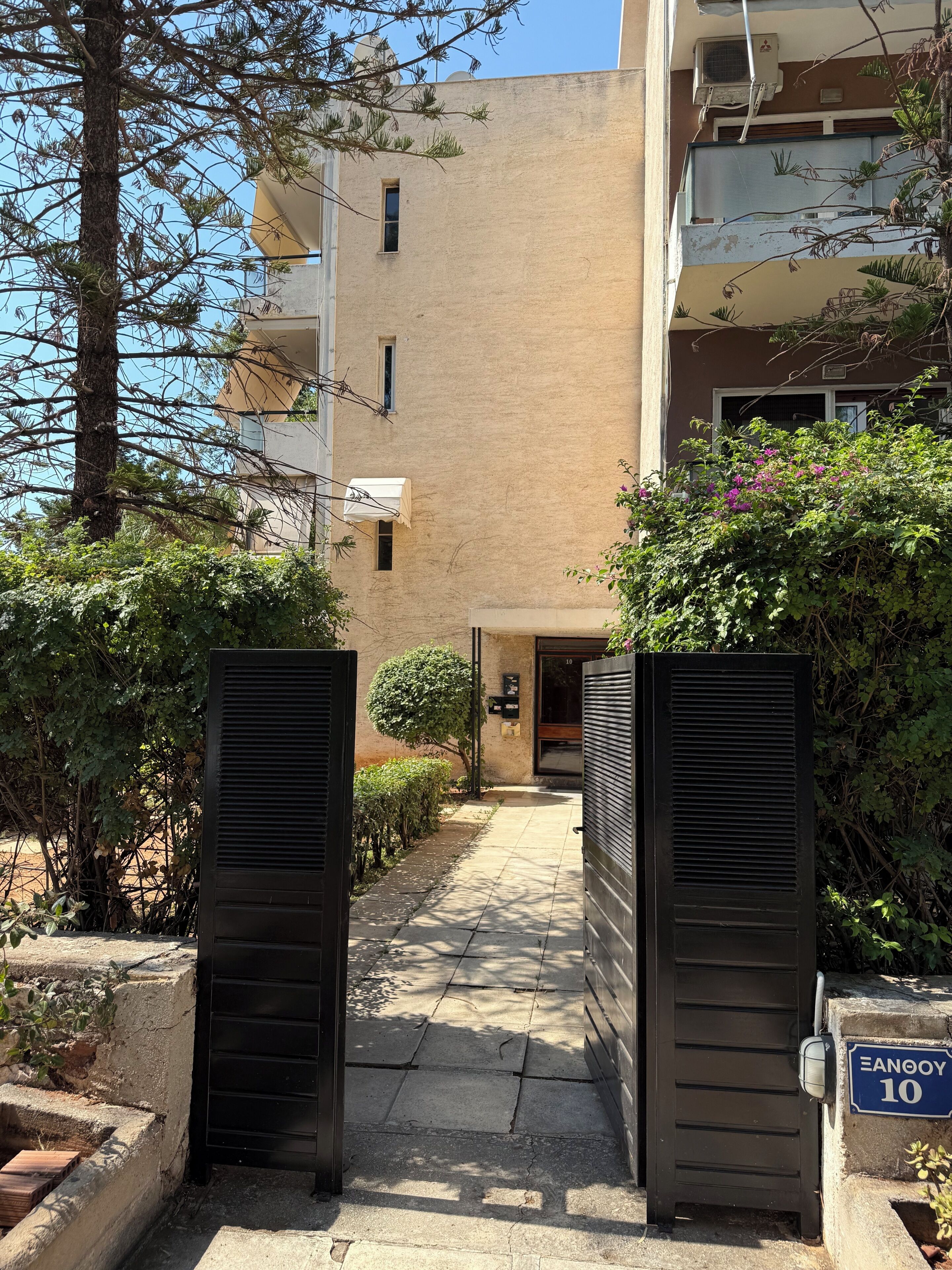 A gated entrance to a building with a clear pathway leading to the door, surrounded by greenery and a clear sky.