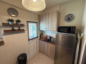 Een compacte keuken met een magnetron, broodrooster en koffiezetapparaat op het aanrecht, een klok aan de muur en een deur met raam.
