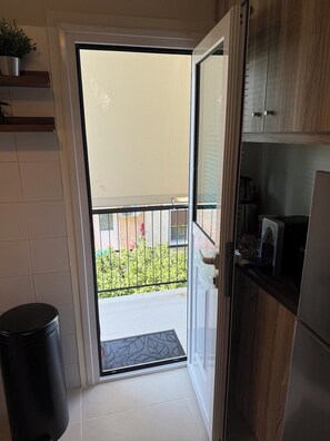 Eine Küche mit einer Schiebetür, die auf einen Balkon führt, einem Mülleimer und einer Mikrowelle auf der Arbeitsfläche.