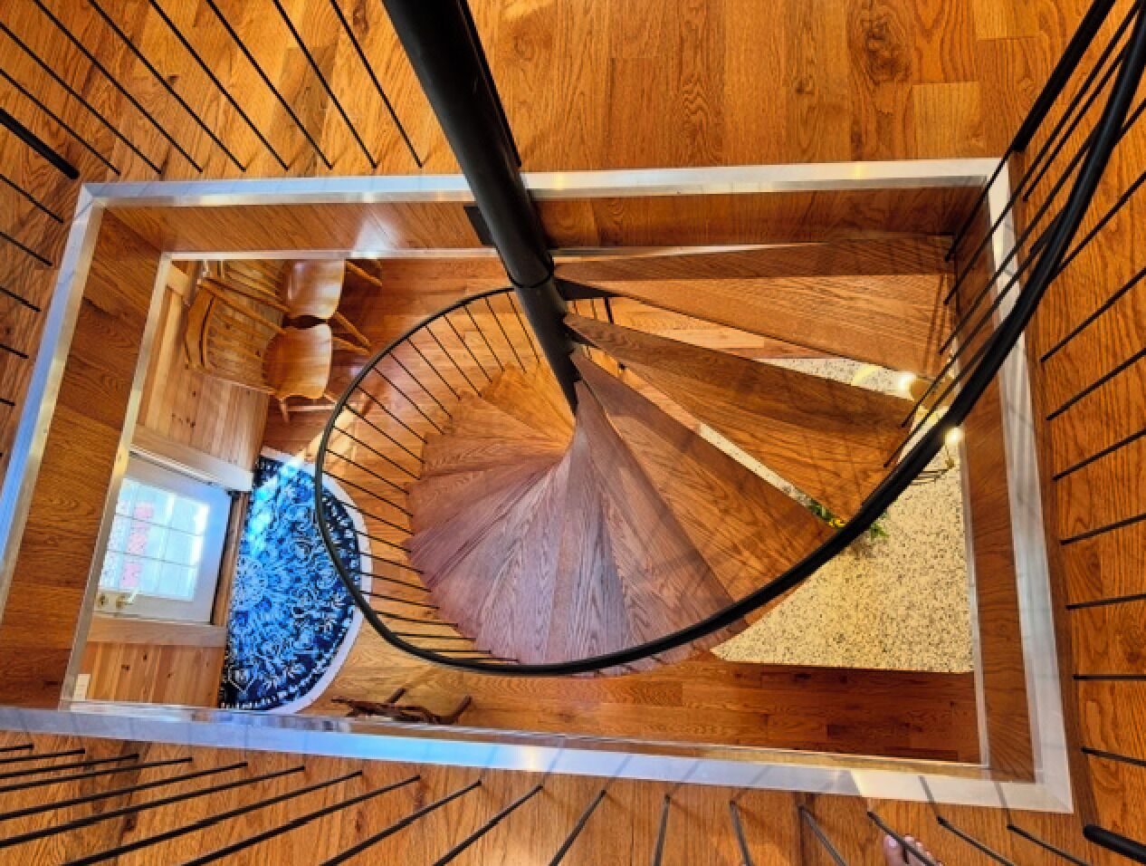 Un escalier en colimaçon avec des marches en bois et des rampes en métal, menant à l’étage supérieur.
