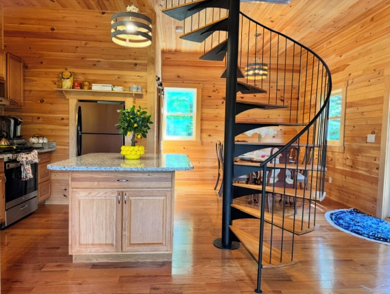 A wooden interior with a kitchen, dining area, and a spiral staircase.