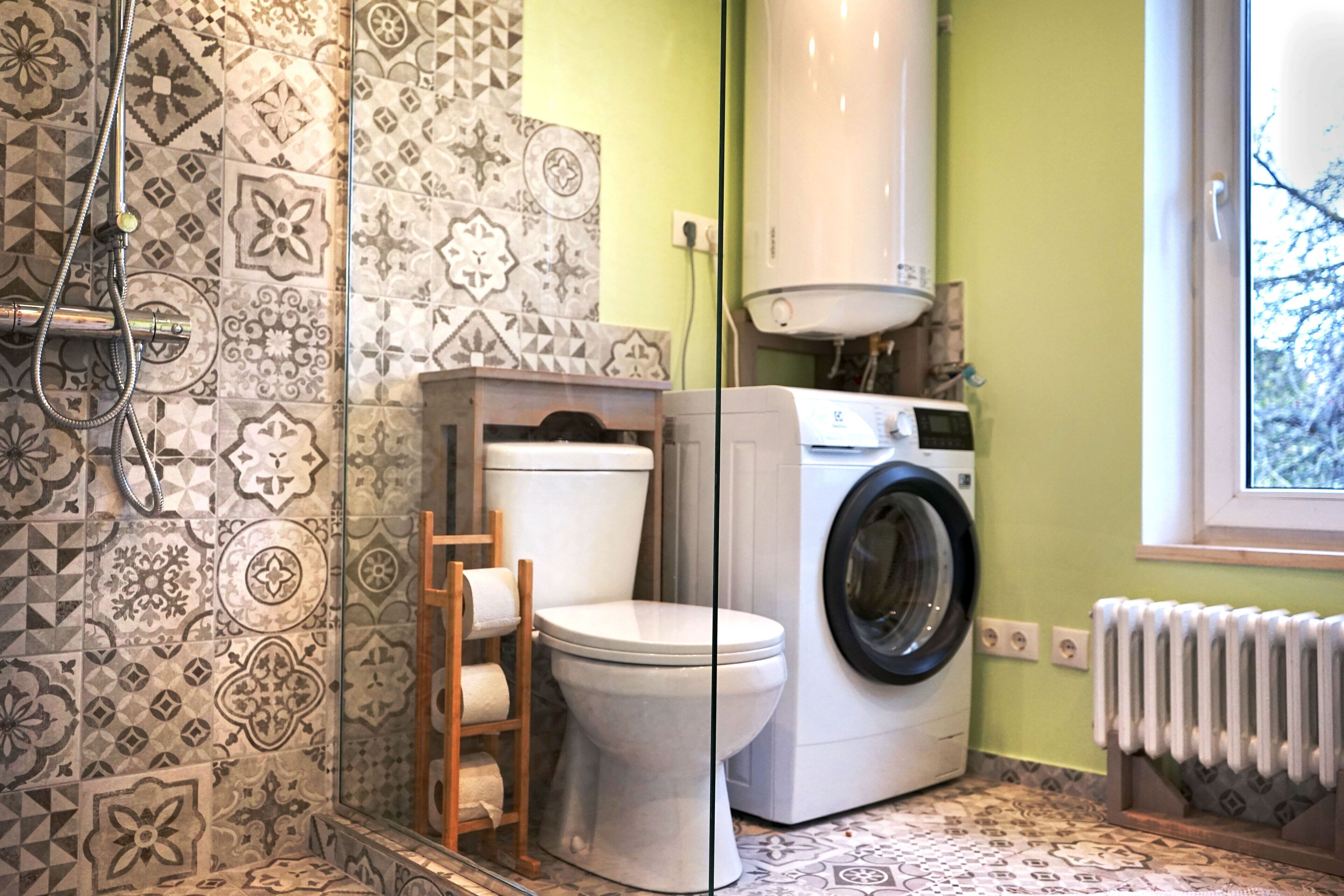Een badkamer met betegelde vloer, toilet, wasmachine en radiator.