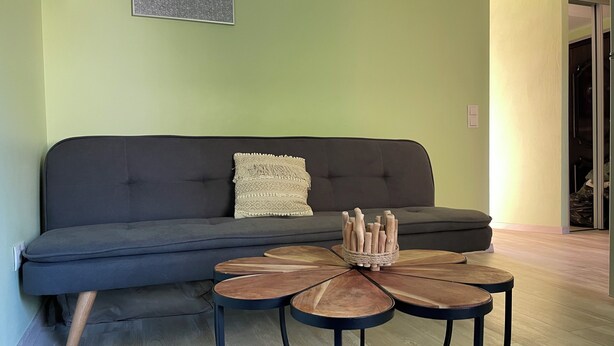 Un salon avec un canapé gris foncé, une table basse ronde ornée d’un élément décoratif tissé, et un mur vert clair.