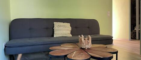 Una sala de estar con un sofá gris oscuro, una mesa de centro redonda con un centro tejido, y una pared verde claro.