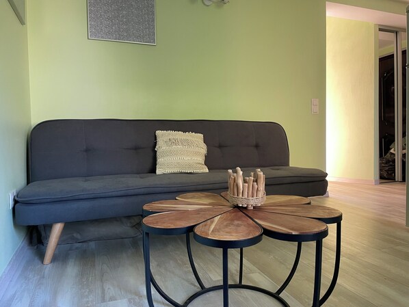 A living room with a dark grey sofa, a round coffee table with a woven centerpiece, and a light green wall.