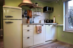 Una cucina con un frigorifero vintage, mobili bianchi, un forno a microonde e una finestra vista alberi.