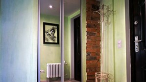Un couloir avec une porte en verre, un radiateur, une œuvre d’art encadrée, un mur de briques et une porte dotée d’une poignée.