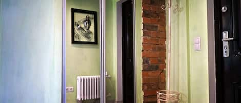 Un pasillo con puerta de cristal, radiador, una obra de arte enmarcada, pared de ladrillo y una puerta con manija.