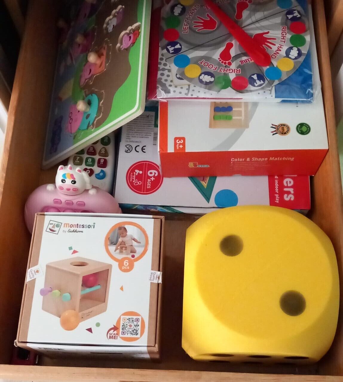 A drawer containing various children's toys and educational materials, including a Montessori toy, a color and shape matching game, and a puzzle.