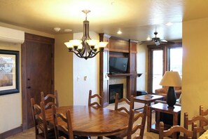 A dining area with a wooden table and chairs, a chandelier, a fireplace, a television, and a ceiling fan. - Beautiful 2 bedroom/bath condo at Grand Lodge on Peak 7 for Oct. 3 - 10! (Breckenridge)
