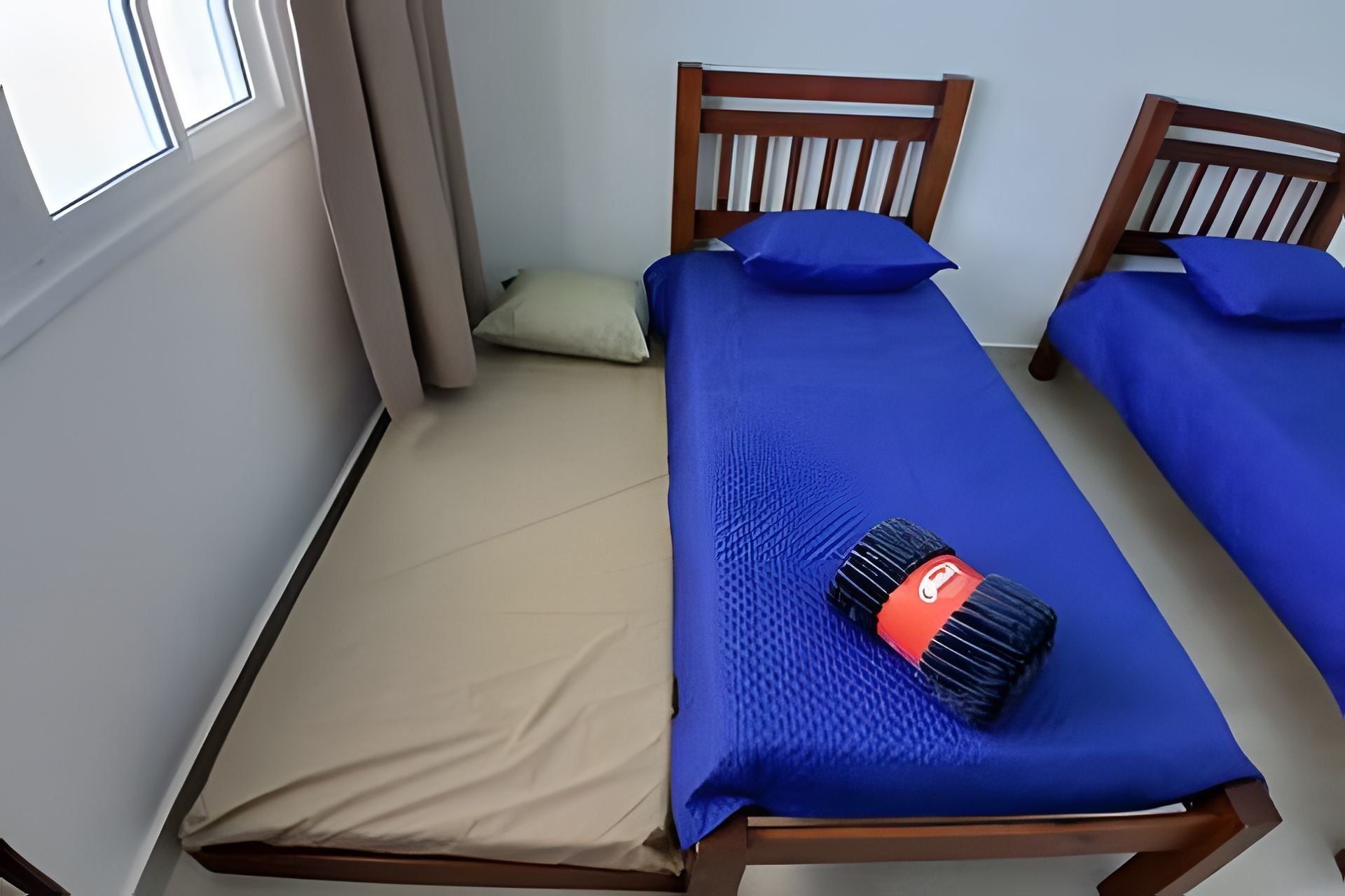 A single bed with a blue bedspread and a red object on it.