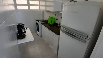 A compact kitchen with white cabinets, a coffee maker, a stove, and a refrigerator.