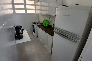 A compact kitchen with white cabinets, a coffee maker, a stove, and a refrigerator. - SHB - Vista incrível  e Pé na Areia  (Guarujá)