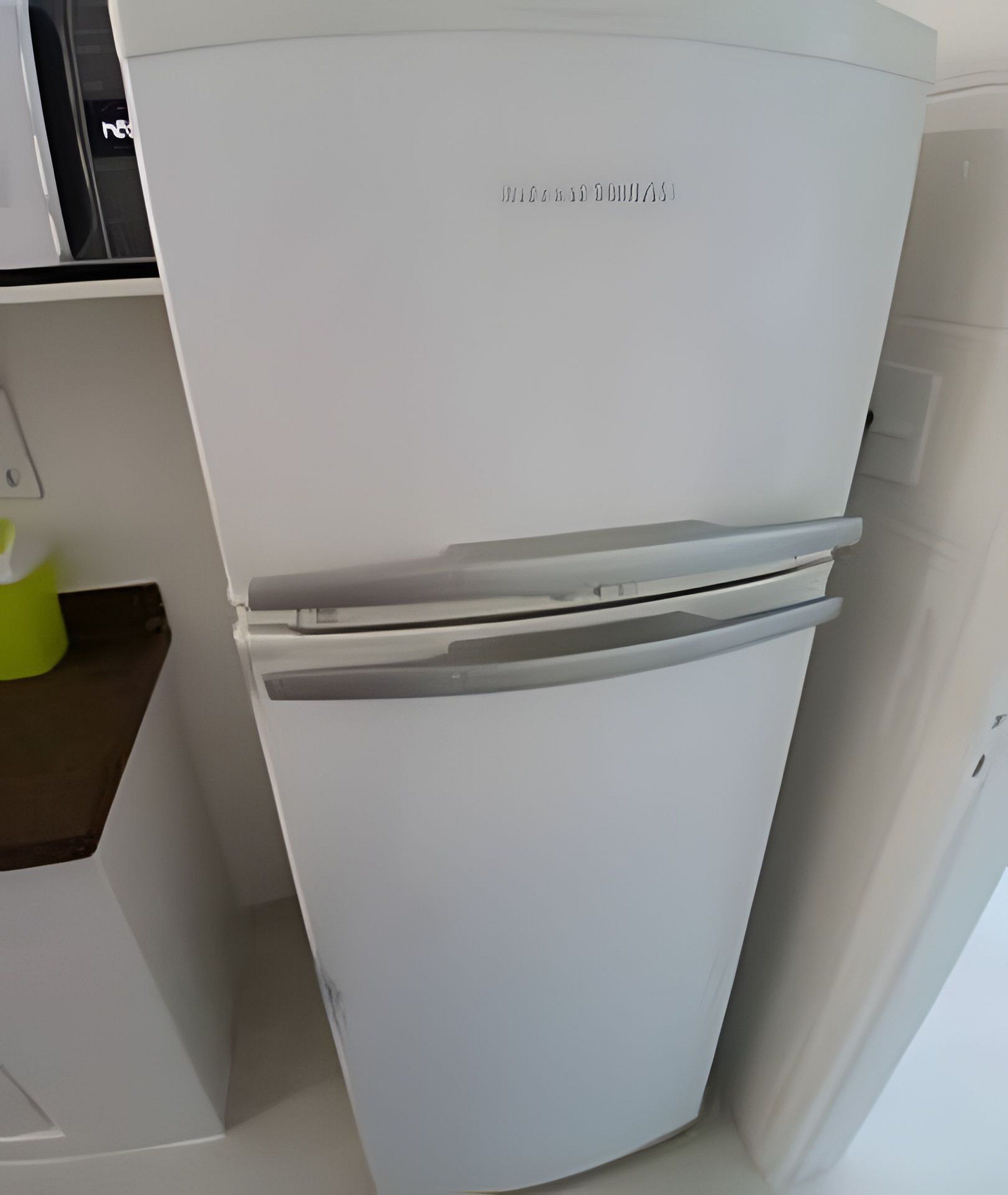 Un réfrigérateur blanc, doté d’un compartiment congélateur situé en haut, se trouve dans une cuisine avec des armoires blanches et un plan de travail marron.