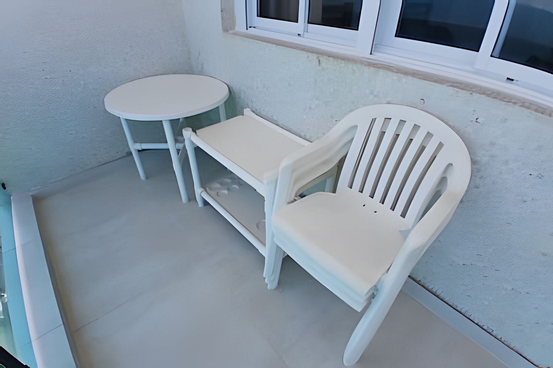 Um pequeno espaço ao ar livre com uma mesa de plástico branca e duas cadeiras de plástico brancas.