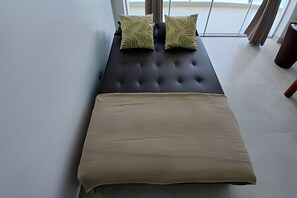 A bed with a dark headboard and two patterned pillows, a beige bedspread, and a view of the outdoors through large windows. - SHB - Vista incrível  e Pé na Areia  (Guarujá)