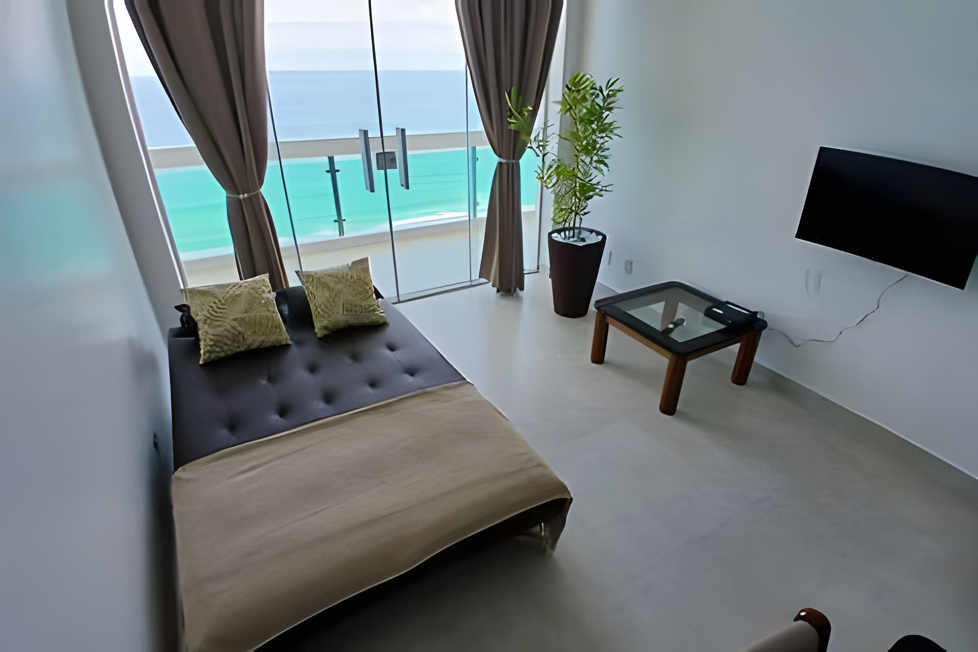 A bedroom with a bed, a TV, a small table, and a view of the ocean.