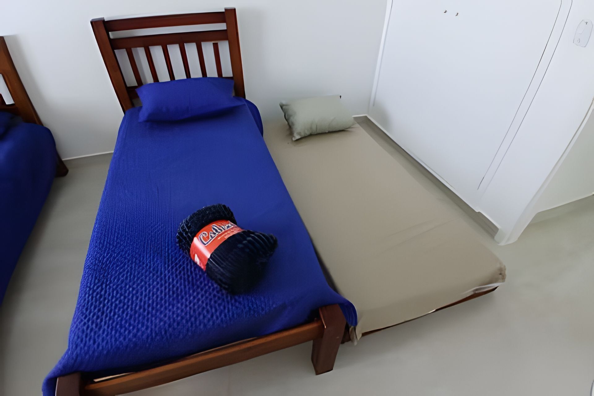 Un lit simple avec une couvre-lit bleue et un oreiller noir orné d’une étiquette rouge.