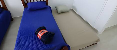 Una cama individual con una colcha azul y un almohadón negro con etiqueta roja.