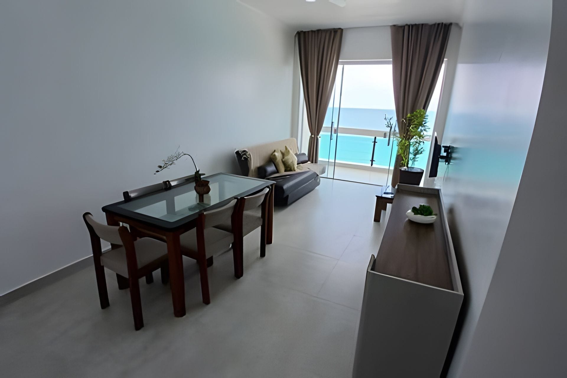 Un salon moderne avec une table à manger en verre, un canapé et une vue sur la mer grâce à de grandes fenêtres.