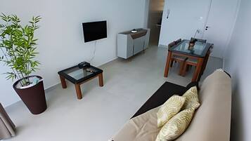 A modern living room with a sofa, a coffee table, a TV, a dining table with chairs, and a potted plant.