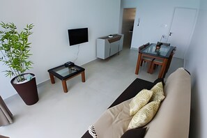 A modern living room with a sofa, a coffee table, a TV, a dining table with chairs, and a potted plant. - SHB - Vista incrível  e Pé na Areia  (Guarujá)