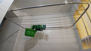 Una cesta de ropa verde colgada de una estructura metálica en una habitación con paredes de azulejos blancos y una pared de acento amarilla.
