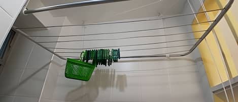 Un panier à linge vert est suspendu à un étagère métallique dans une pièce dont les murs sont recouverts de carreaux blancs, avec un mur d’accent jaune.